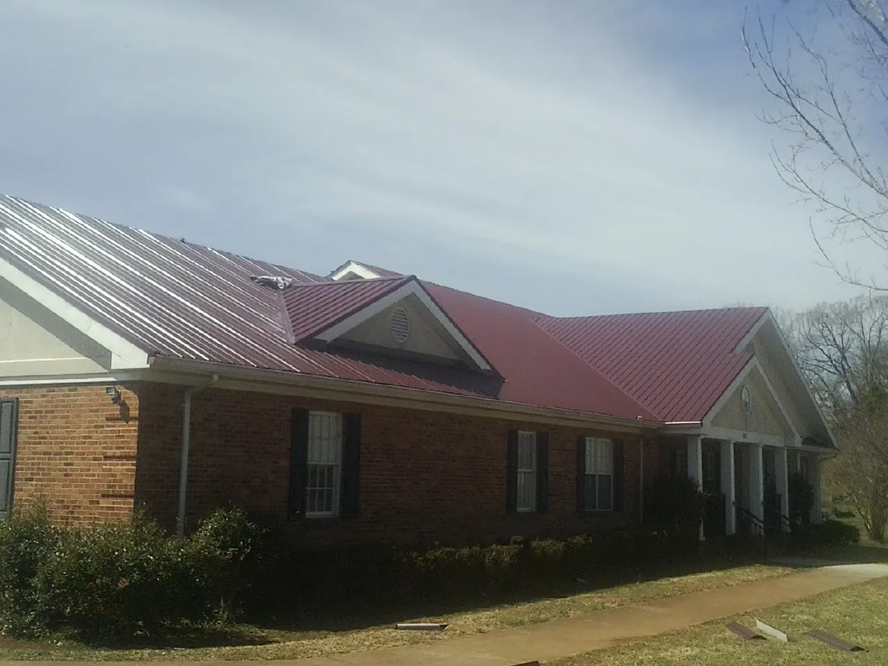 Red metal roof with gabled entries on a long brick building, from a Hail Damage Roof Repair job in Siletz