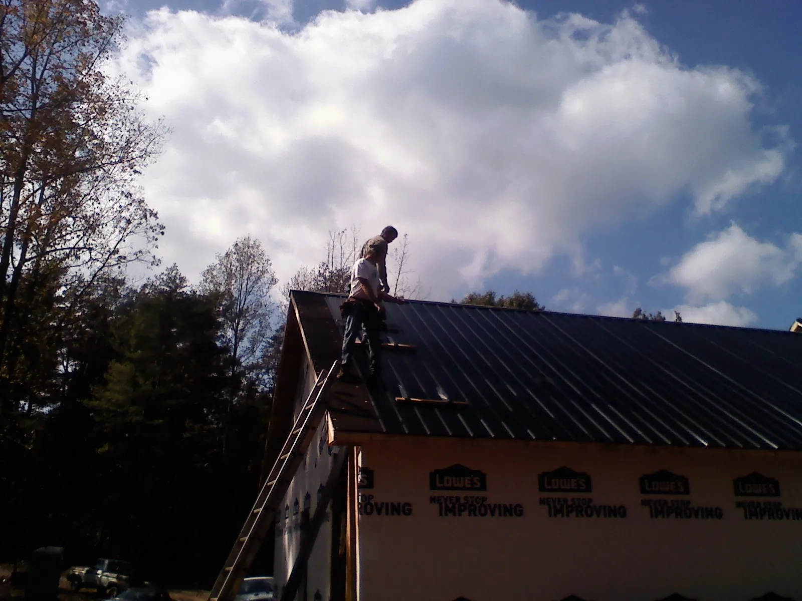 Roofer fastening dark metal panels high against a cloudy sky, from a Roof Inspection job in Siletz